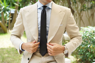 Model wearing an OTAA Bond Black Skinny Tie with a white shirt and cream suit