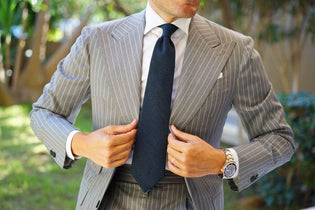 Navy tie worn with a white shirt and grey pinstriped suit outdoors.